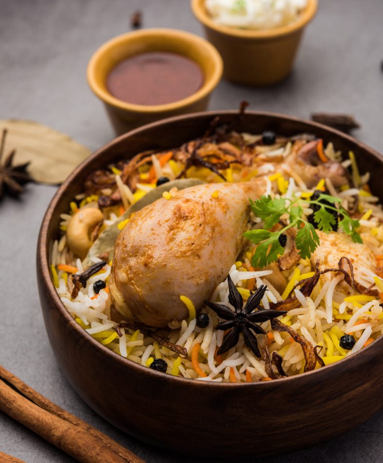 Restaurant style Spicy Chicken Biryani in wooden bowl with Raita and salan, Popular Indian or Pakistani Food