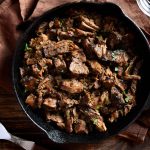 Close up view of slow cooked pulled beef in cast iron pan on wooden table. Top view, flat lay