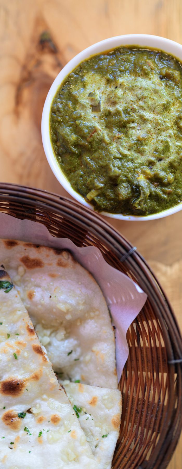 Top view of Indian food palak paneer spinach curry served with garlic naan bread on a wooden table